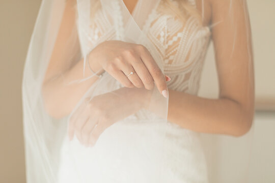 Crop photo of unrecognisable bride hands wearing white wedding dress and bridal veil while preparing for her wedding day