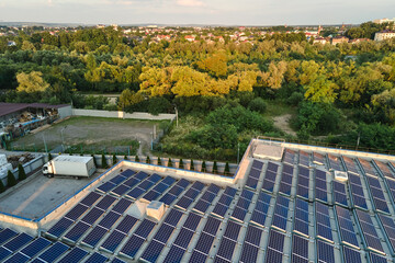 Aerial view of blue photovoltaic solar panels mounted on industrial building roof for producing...