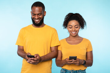 Young black couple using cellphones, surfing web, posting in social media, checking email messages...