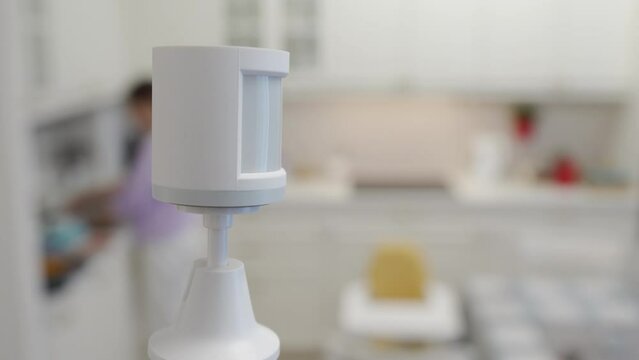 Smart home wireless motion sensor for alarm system and smart home automation, small plastic white motion detector installed in the living room. High quality 4k footage