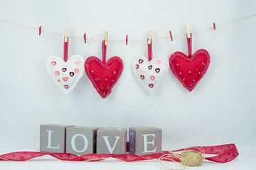 Walentynkowe tło, wiszące białe i czerwone serca i napis z drewnianych brył z liter tworzące słowo love.