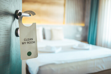 Opened door of hotel room. Door of hotel room with please make up room sign. Hotel room or apartment doorway with key and keyring key fob in open door and bedroom in background