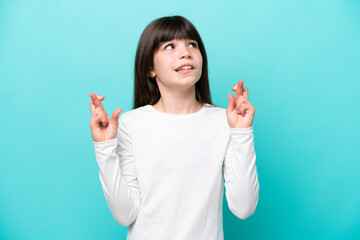 Fototapeta premium Little caucasian girl isolated on blue background with fingers crossing and wishing the best