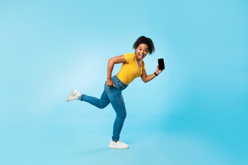 Happy young Afro woman with empty smartphone running on blue background, mockup for website or mobile app