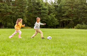 childhood, leisure games and people concept - happy little boy and girl with ball playing soccer at summer park