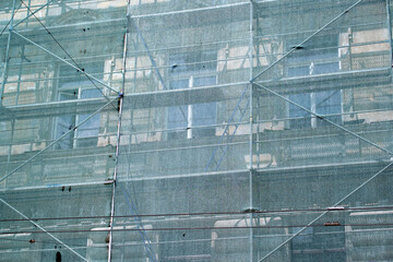 Building facade under renovation works with construction scaffolding frame covered with protective net for workers safety