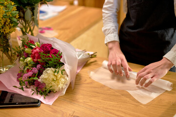 Obraz na płótnie Canvas woman florist at work arranging various flowers in bouquet, decorating bouquet. close-up hands of young lady in apron standing behind desk making bouquet of fresh flowers. focus on hands. beauty