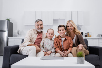happy couple and grandchildren sitting on couch in kitchen and looking at camera.