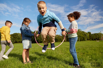 childhood, leisure and people concept - group of happy children playing game with hula hoop at park - obrazy, fototapety, plakaty