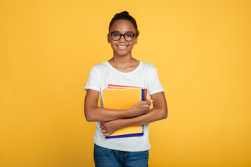 Cheerful teenage african american girl pupil in glasses and casual holds books and ready to learn