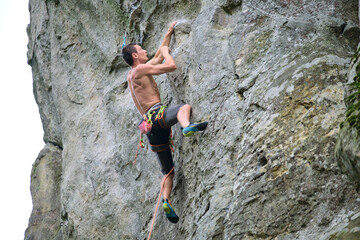 Strong male climber climbing steep wall of rocky mountain. Sportsman overcoming difficult route. Engaging in extreme sports hobby concept