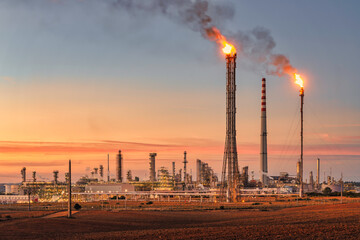 Sines refinery, Portugal at sunset with chimneys giving off flames and smoke.