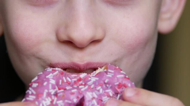 Caucasian cheerful boy 7 years old bites off an appetizing sweet donut, Macro. The child's mouth eats a sweet dessert, parts of the child's face. Slow motion. selective focus