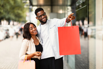 Portrait of black couple with shopping bags pointing at window