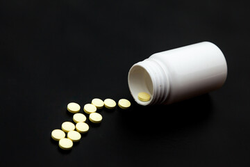 White plastic jar on a black background with poured pills.