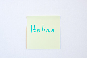 Top view flat lay of the reminder notepaper of yellow color with word Italian on it on white background. Flashcards and language studies concept