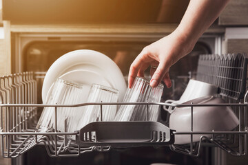 Female hand loading dished, empty out or unloading dishwasher with utensils. Kitchen appliances,...