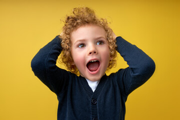 Portrait of excited little boy with curly hair screaming, having crazy expression, surprised by...