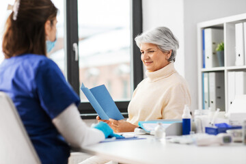 medicine, health and vaccination concept - doctor or nurse and senior woman reading medical...