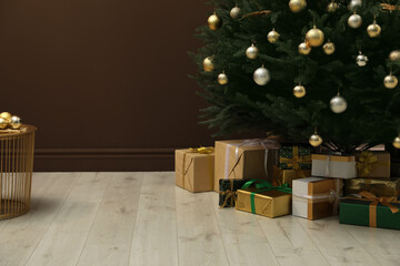 Beautifully decorated Christmas tree and many gift boxes near brown wall indoors, space for text