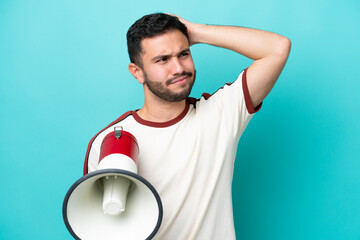 Young Brazilian man isolated on blue background holding a megaphone and having doubts