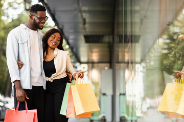 Black couple with shopping bags pointing at window