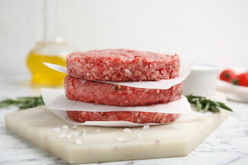 Raw hamburger patties with rosemary and salt on white marble table, closeup