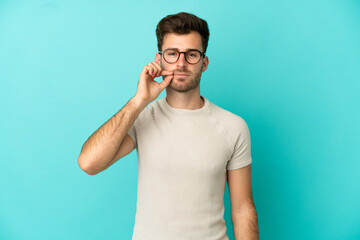 Young caucasian handsome man isolated on blue background showing a sign of silence gesture