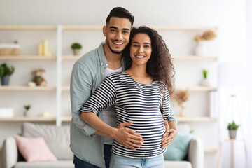 Fototapeta premium Happy middle-eastern man hugging his beautiful pregnant wife, posing together