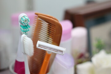 Toothbrush, comb, razor are in the glass, placed in the bathroom in front of the mirror.