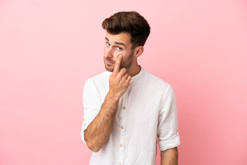 Young caucasian handsome man isolated on pink background showing something