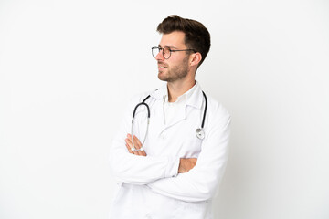 Fototapeta premium Young doctor caucasian man over isolated on white background wearing a doctor gown and with arms crossed looking side