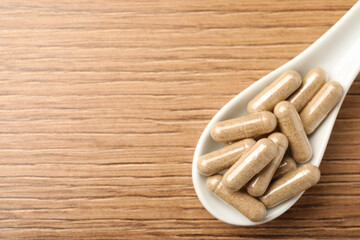 Spoon with dietary supplement capsules on wooden table, top view. Space for text