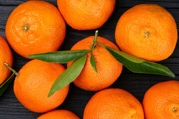 Top view of whole  ripe fresh citrus fruits tangerines with green leaves on black background.