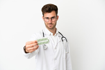 Young doctor caucasian man over isolated on white background wearing a doctor gown and holding pills