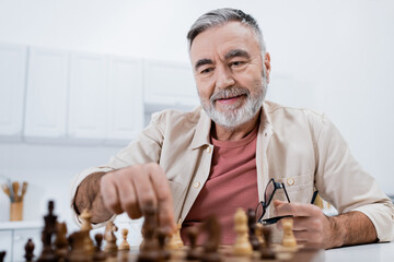 smiling senior man playing chess in kitchen at home.
