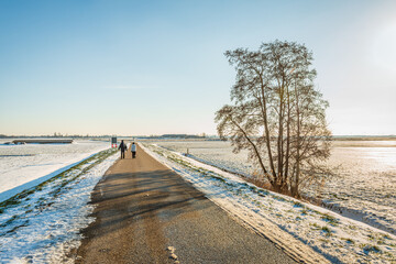 A man and a woman are walking together on a country road in a Dutch polder. It is winter, the sun is low and the fields are covered with snow.