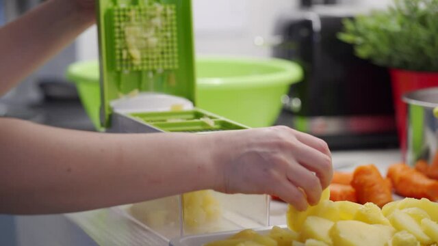 Woman cooking in the kitchen using a vegetable chopper with container, chop and slice boiled potatoes with food slicer on kitchen countertop closeup. High quality 4k footage