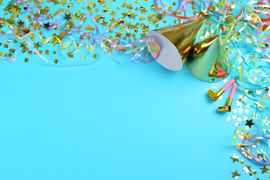 Colorful serpentine streamers, party horns, hats and confetti on light blue background, above view. Space for text