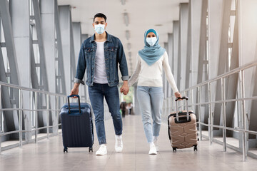 Travels During Pandemic. Islamic Couple Wearing Masks Walking With Suitcases At Airport