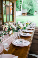 A beautiful outdoor wedding setting in pink flowers. plates and cutlery on a wooden table against a backdrop of greenery. On a Summer day 
a wooden reception table in the backyard, decorated with rose