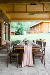 A beautiful outdoor wedding setting in pink flowers. plates and cutlery on a wooden table against a backdrop of greenery. On a Summer day 
a wooden reception table in the backyard, decorated with rose