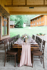 A beautiful outdoor wedding setting in pink flowers. plates and cutlery on a wooden table against a backdrop of greenery. On a Summer day 
a wooden reception table in the backyard, decorated with rose
