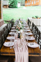 A beautiful outdoor wedding setting in pink flowers. plates and cutlery on a wooden table against a backdrop of greenery. On a Summer day 
a wooden reception table in the backyard, decorated with rose