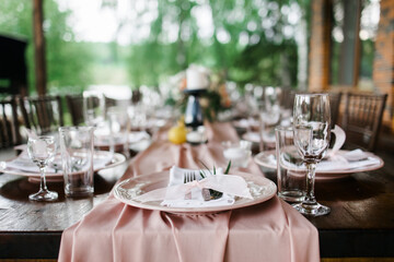 A beautiful outdoor wedding setting in pink flowers. plates and cutlery on a wooden table against a backdrop of greenery. On a Summer day 
a wooden reception table in the backyard, decorated with rose