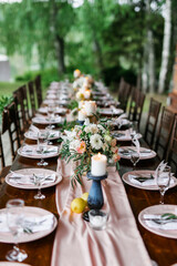 A beautiful outdoor wedding setting in pink flowers. plates and cutlery on a wooden table against a backdrop of greenery. On a Summer day 
a wooden reception table in the backyard, decorated with rose