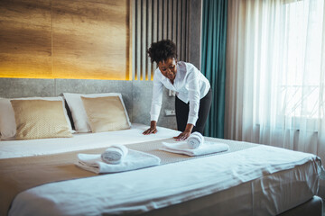 Young chambermaid making bed in hotel room. Young hotel maid setting up white pillow on bed sheet in hotel room. Young maid arranging blanket on bed in hotel room