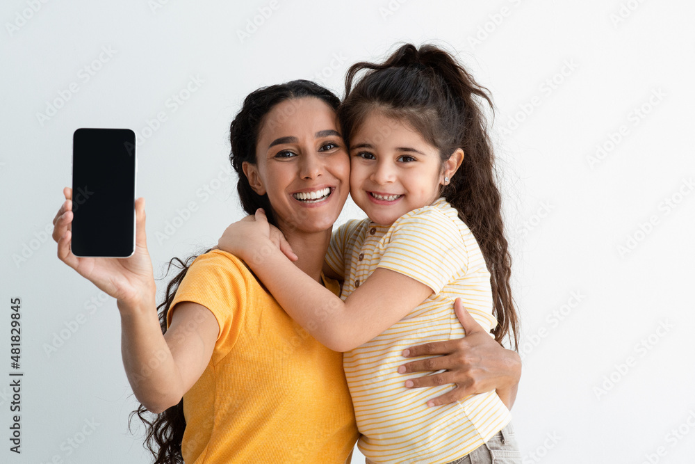 Wall mural Cheerful Arab Mother And Daughter Demonstrating Smartphone With Black Screen At Camera