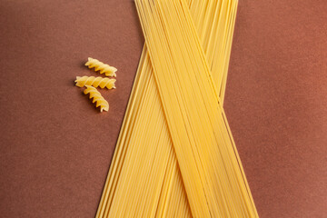 uncooked spaghetti and fushilli on brown background