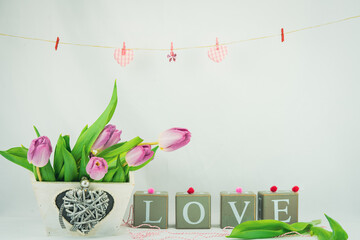 Walentynkowe tło, różowe tulipany w pudełku drewnianym z serduszkiem i napis z brył drewnianych układające się w sowo love, zawieszone na sznurku serduszka.